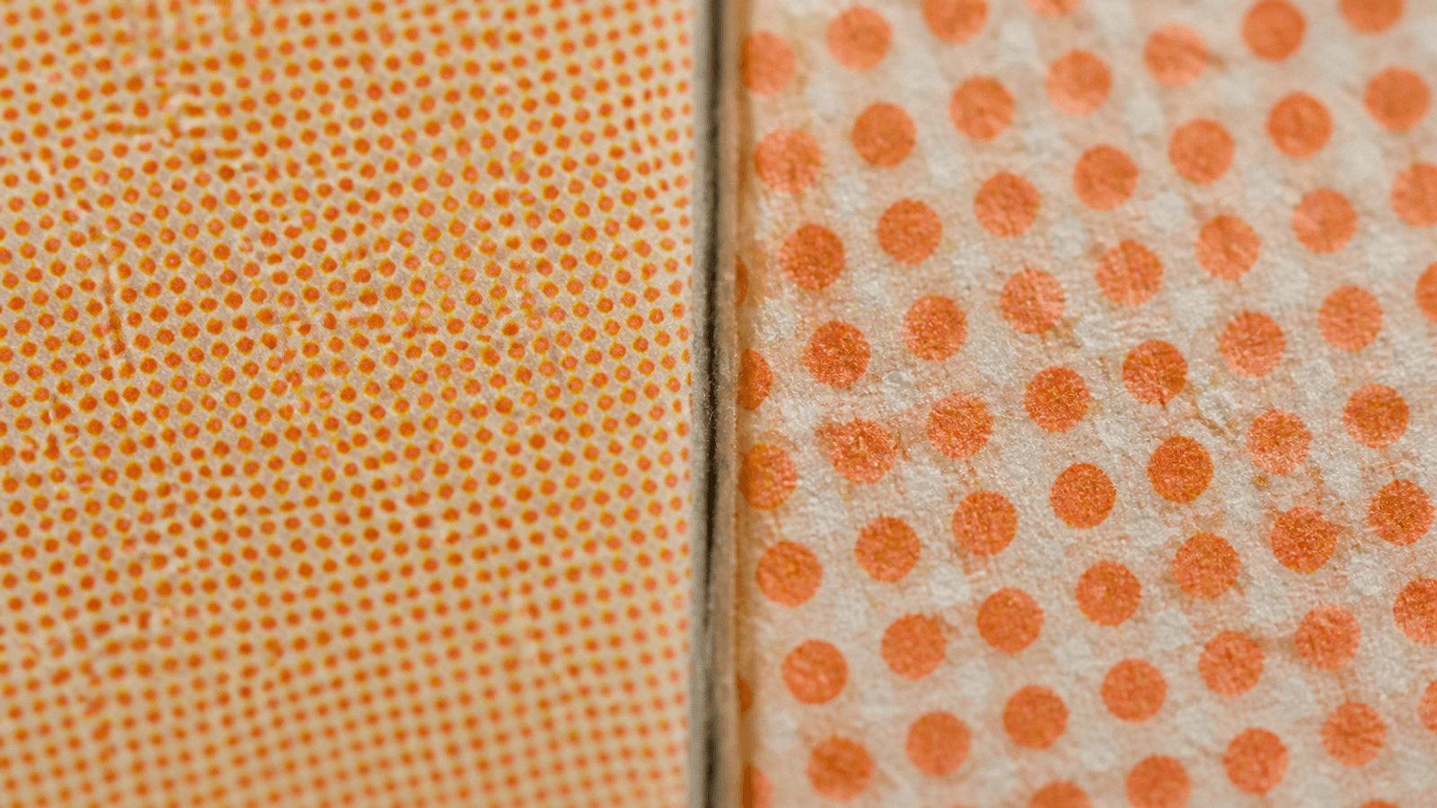Extreme macro photograph showing two adjacent printed paperboard surfaces side-by-side, left with fine offset halftone dots in a sharp pattern and right with coarser flexo dots showing slightly less crispness, natural color with paperboard texture visible